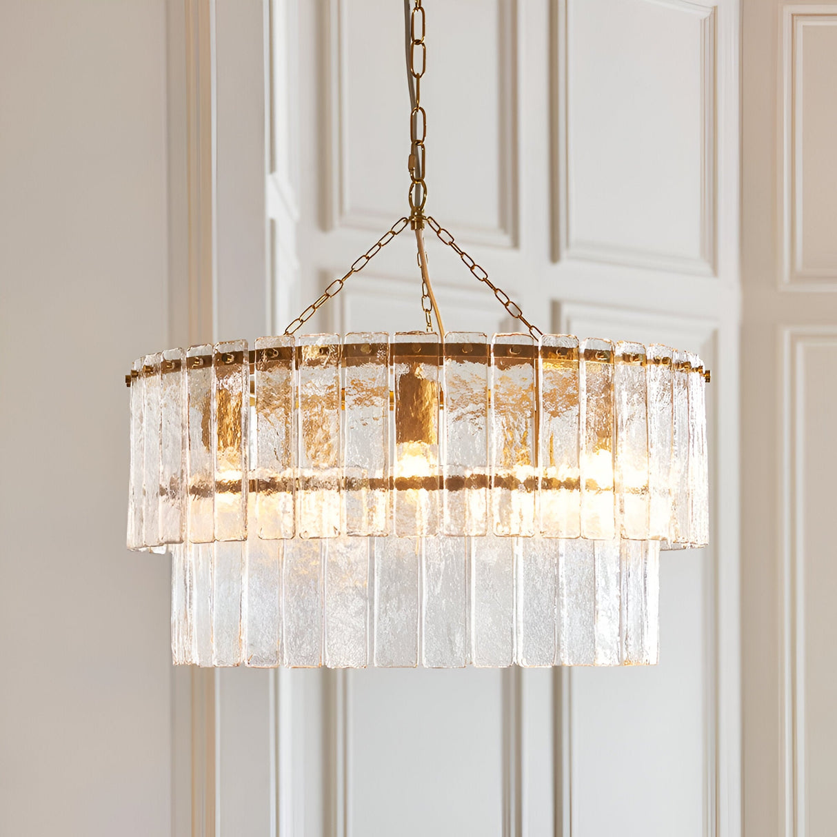 Endon Brockhurst 5 light chandelier in brushed aged brass with two tiers of textured glass panels, suspended from a chain against pale panelled doors.