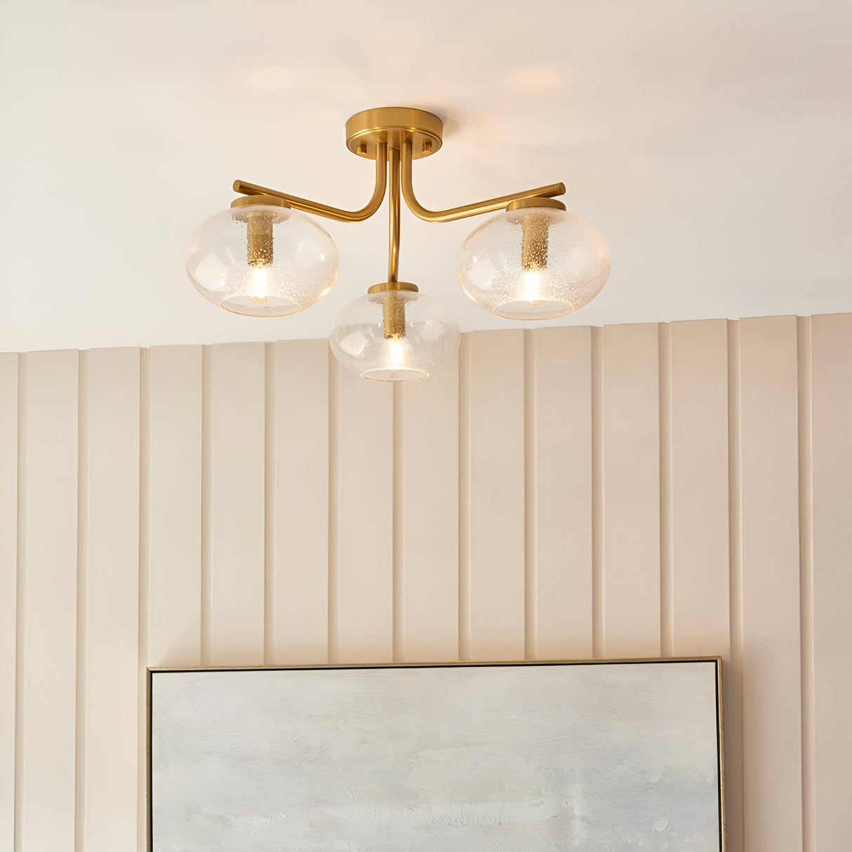 Pemberton 3 Light Semi-Flush Ceiling Light in brass with clear bubble glass shades, shown on a panelled wall above framed artwork.