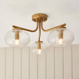 Pemberton 3 Light Semi-Flush Ceiling Light in brass with clear seeded glass globe shades, mounted on a panelled wall in a room setting.