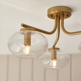 Pemberton 3 Light Semi-Flush Ceiling Light in brass, close-up of curved arms and bubbled glass globe shades with visible bulbs, set against a light ceiling.