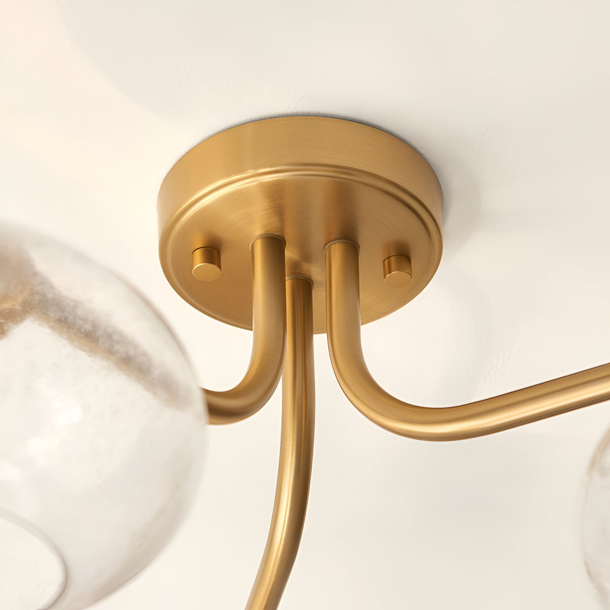 Close-up of the Pemberton 3 Light Semi-Flush Ceiling Light in brass, showing curved metal arms and round ceiling plate with glass shades.