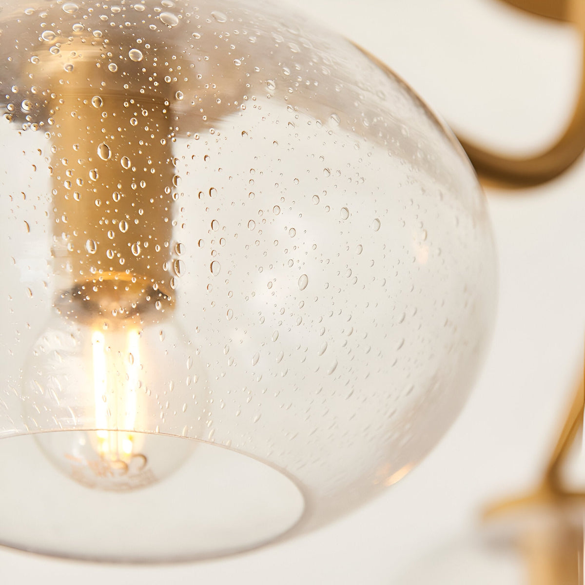 Close-up of the Pemberton 3 Light Semi-Flush Ceiling Light in brass, showing a seeded glass shade, brass fitting, and lit E14 bulb against a white background.