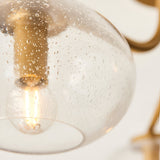 Close-up of the Pemberton 3 Light Semi-Flush Ceiling Light in brass, showing a seeded glass shade, brass fitting, and lit E14 bulb against a white background.