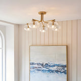 Endon Pemberton 5 light semi-flush ceiling light in brass with five clear glass globe shades, mounted above a framed coastal artwork in a hallway.