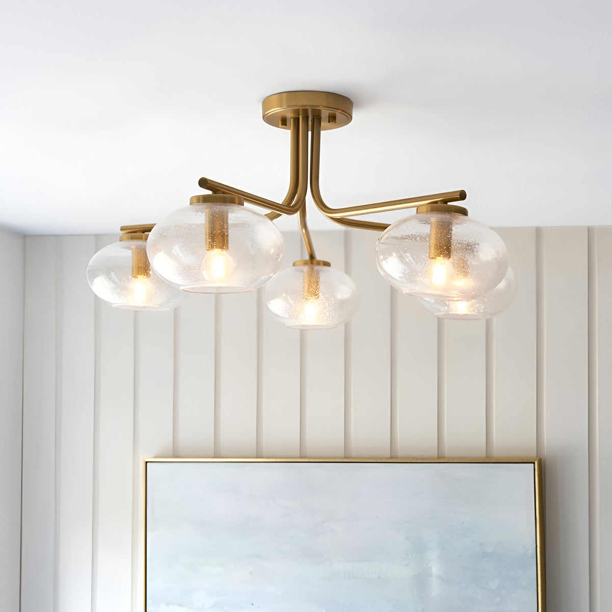 Endon Pemberton 5 light semi-flush ceiling light in brass with rounded seeded glass shades on curved arms, mounted above a framed mirror.