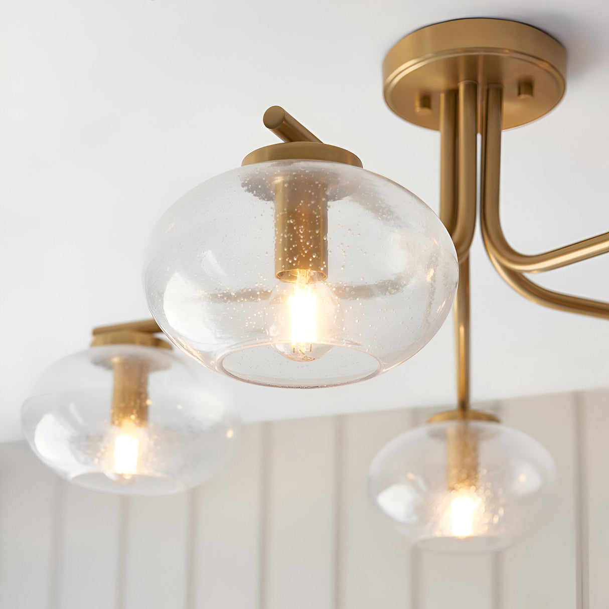 Endon Pemberton semi-flush ceiling light in brass, shown close-up with three of its five seeded glass globe shades on curved arms lit warmly.