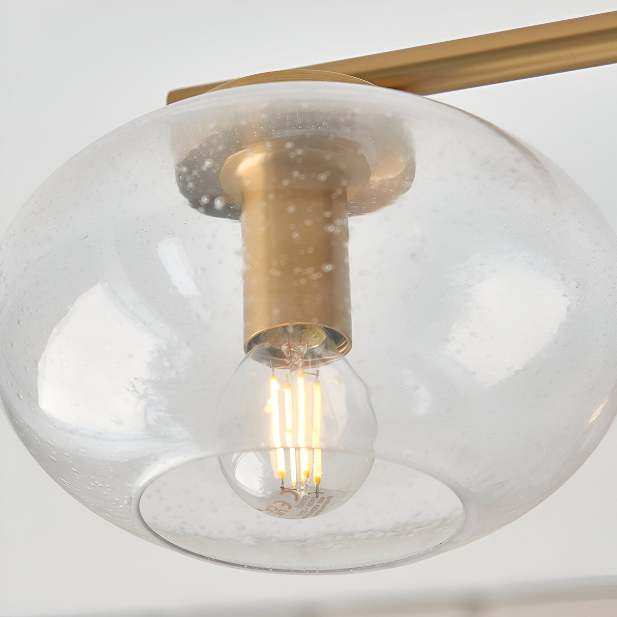 Close-up of one clear seeded glass globe shade on the Endon Pemberton semi-flush ceiling light, showing the brass arm and E14 filament lamp inside.