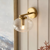 Endon Pemberton brass wall light with a hand-blown clear bubbled glass oval shade, mounted on a panelled wall beside a framed artwork.