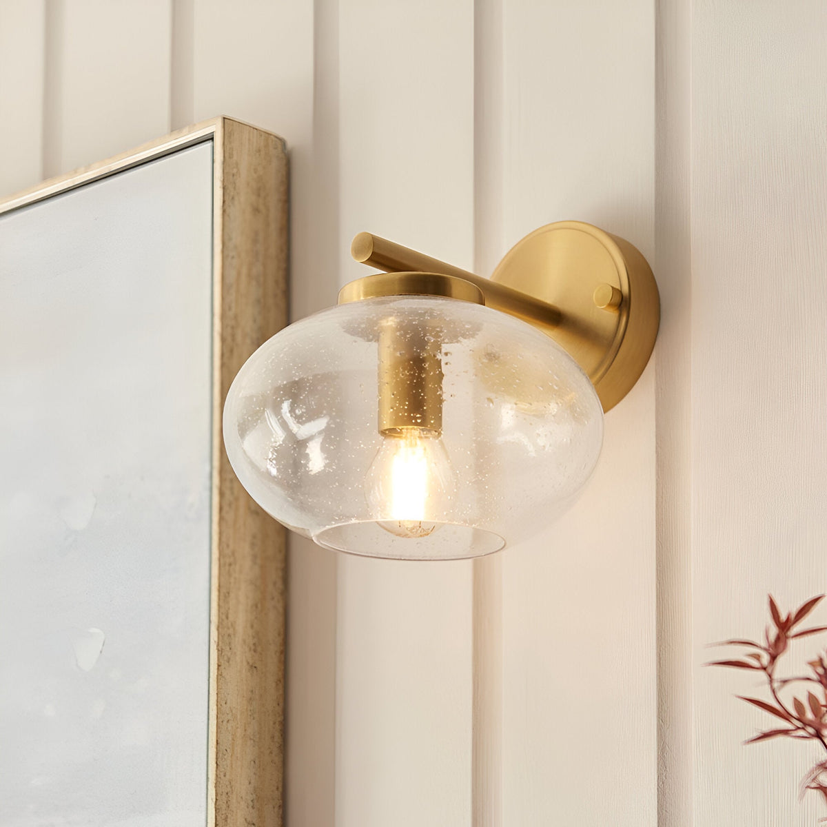 Endon Pemberton wall light in brass with a bubbled clear glass oval shade, mounted beside a wood-framed mirror on panelled cream walls.