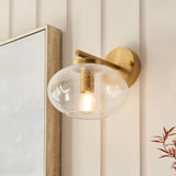 Endon Pemberton wall light in brass with a bubbled clear glass oval shade, mounted beside a wood-framed mirror on panelled cream walls.