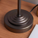 Close-up of the Endon Chartworth table lamp's bronze stepped, tapering base on a wooden surface, with the black cable visible behind.