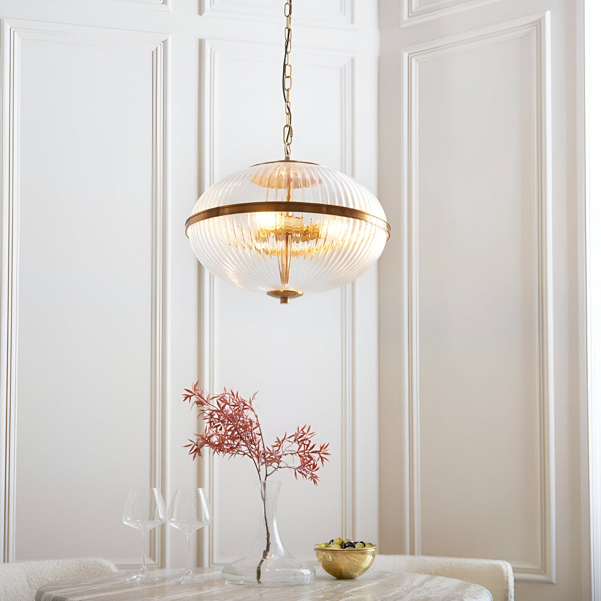 Langton 3 Light Pendant in brass with ribbed glass globe on chain, hanging in a panelled dining room above a table setting.