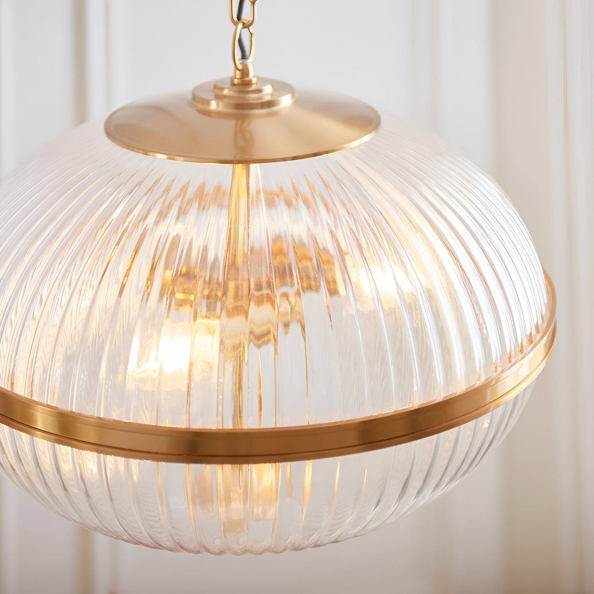 Langton 3 Light Pendant in brass, close-up of ribbed clear glass globe with brass band and ceiling rose, chain suspension visible.