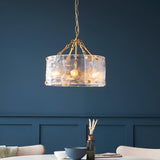 Brockmont 4-Light Pendant in brass with a cylindrical drum shade, textured glass panels, and chain suspension, lit above a dining table.