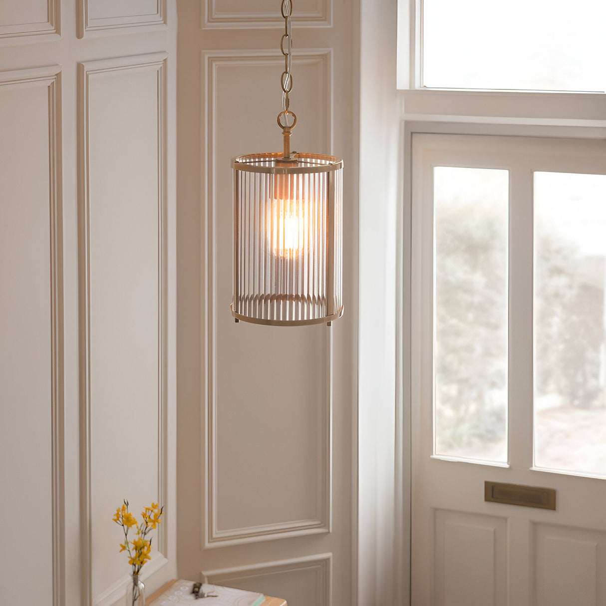 Endon Rothbury pendant light with ribbed clear glass cylindrical shade and antique brass frame, hung on a chain in a panelled hallway by a door.