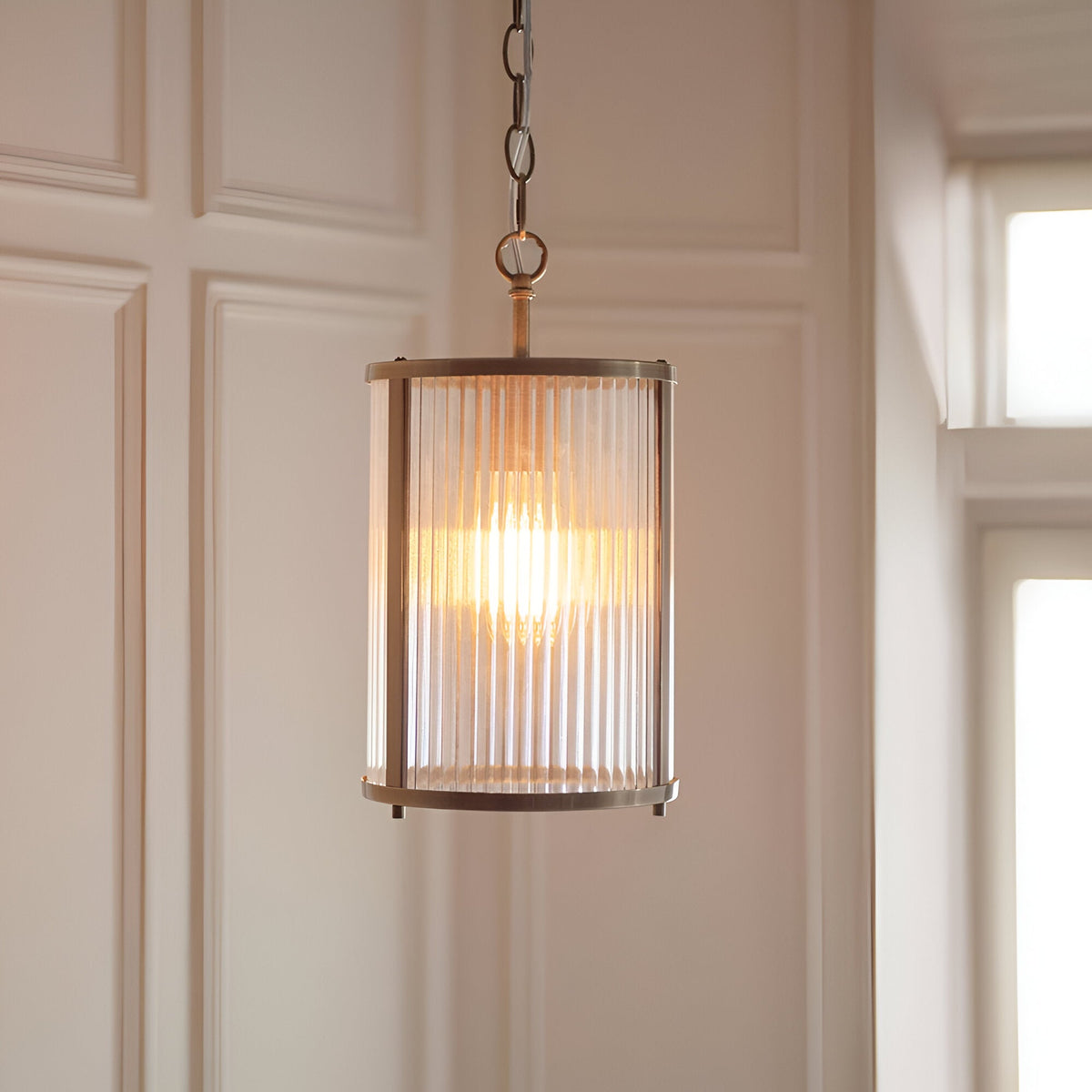 Endon Rothbury pendant with a ribbed clear glass cylindrical shade and antique brass frame, suspended from a chain in a panelled hallway.