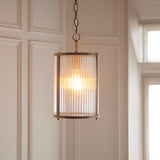 Endon Rothbury pendant with a ribbed clear glass cylindrical shade and antique brass frame, suspended from a chain in a panelled hallway.