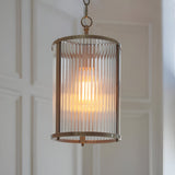 Endon Rothbury pendant light with a ribbed clear glass cylindrical shade and antique brass frame, hung from a chain against a panelled wall.