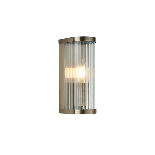 Endon Rothbury wall light with curved antique brass frame and vertically ribbed clear glass diffuser, single E14 lamp illuminated, on a white background.