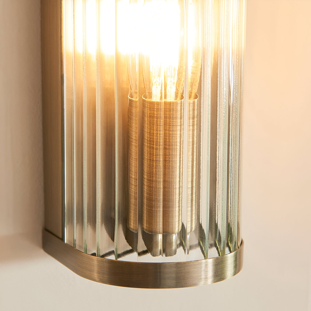 Close-up of the Endon Rothbury wall light showing its antique brass fitting and vertically ribbed clear glass diffuser with a warm E14 filament bulb.