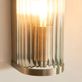 Close-up of the Endon Rothbury wall light showing its antique brass fitting and vertically ribbed clear glass diffuser with a warm E14 filament bulb.