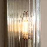 Close-up of Endon Rothbury wall light showing lit E14 candle bulb behind vertically ribbed fluted clear glass with antique brass fitting.