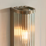 Rothbury 2 Light Wall Light in antique brass with ribbed clear glass diffusers, mounted on a light wall, showing a lit exposed bulb.