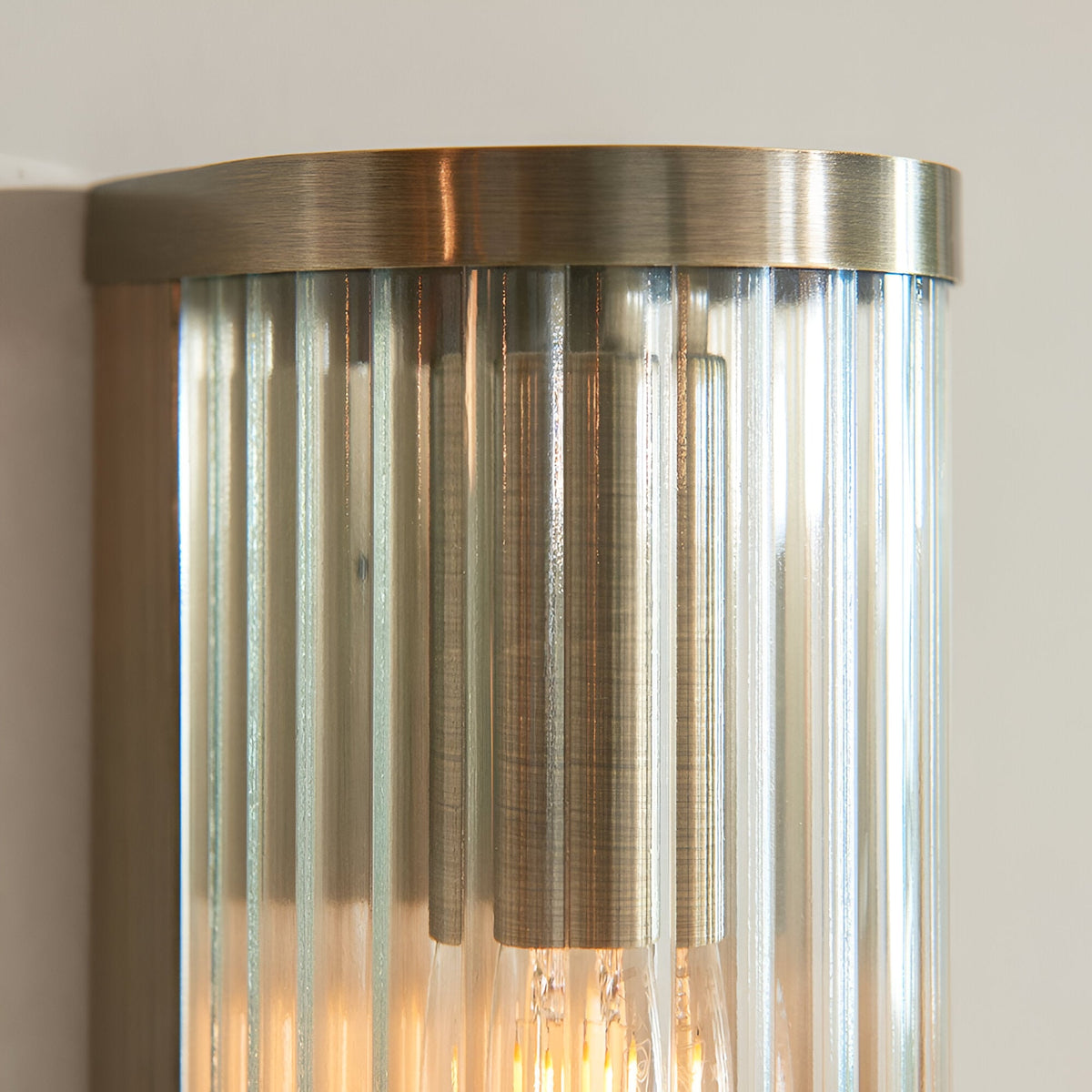 Close-up of the Rothbury 2 Light Wall Light in antique brass, showing the brushed metal cap and vertically ribbed clear glass diffusers with visible bulbs.