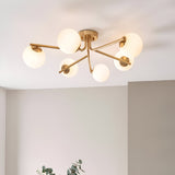 Grantham 6 Light Semi-Flush Ceiling Light in aged brass with six branching arms and round opal glass globe shades, shown illuminated on a light ceiling.