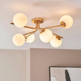 Grantham 6 Light Semi-Flush Ceiling Light in aged brass with six white glass globe shades on angled arms, shown mounted on a light-coloured ceiling.