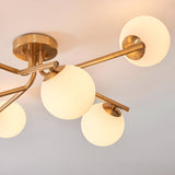 Grantham 6 Light Semi-Flush Ceiling Light in aged brass, close-up of branching arms holding round opal glass globe shades, against a light background.
