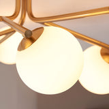 Close-up of the Grantham 6 Light Semi-Flush Ceiling Light, showing aged brass arms and round opal glass globe shades against a pale ceiling.