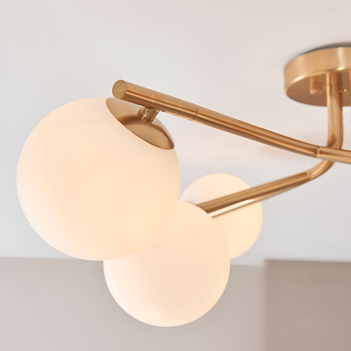 Close-up of the Grantham 6 Light Semi-Flush Ceiling Light in aged brass, showing angled arms and three opal glass globe shades against a plain ceiling.