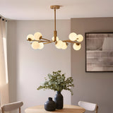Grantham 10 Light Pendant in brushed aged brass with matt opal glass spheres on angled arms, shown above a dining table with vases and greenery.