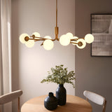 Grantham 10 Light Pendant in brushed aged brass, with matt opal glass spheres on branching arms, hung above a dining table in a neutral-toned room.