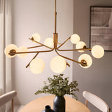 Grantham 10 Light Pendant in brushed aged brass with ten matt opal glass globes on angled arms, shown above a dining table.