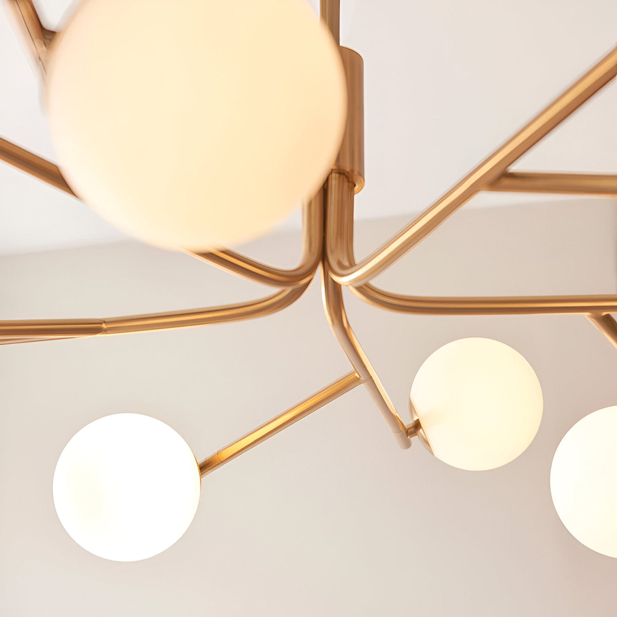 Close-up of the Grantham 10 Light Pendant in brushed aged brass, showing branching metal arms and matt opal glass spheres against a light ceiling.