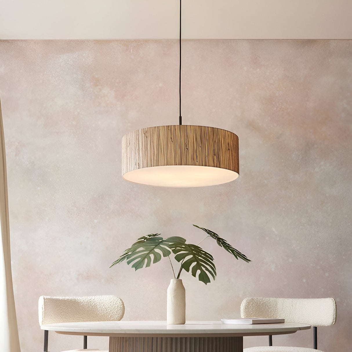 Endon Salcombe pendant light with woven natural seagrass drum shade and black cable, hanging above a dining table with monstera leaves in a vase.