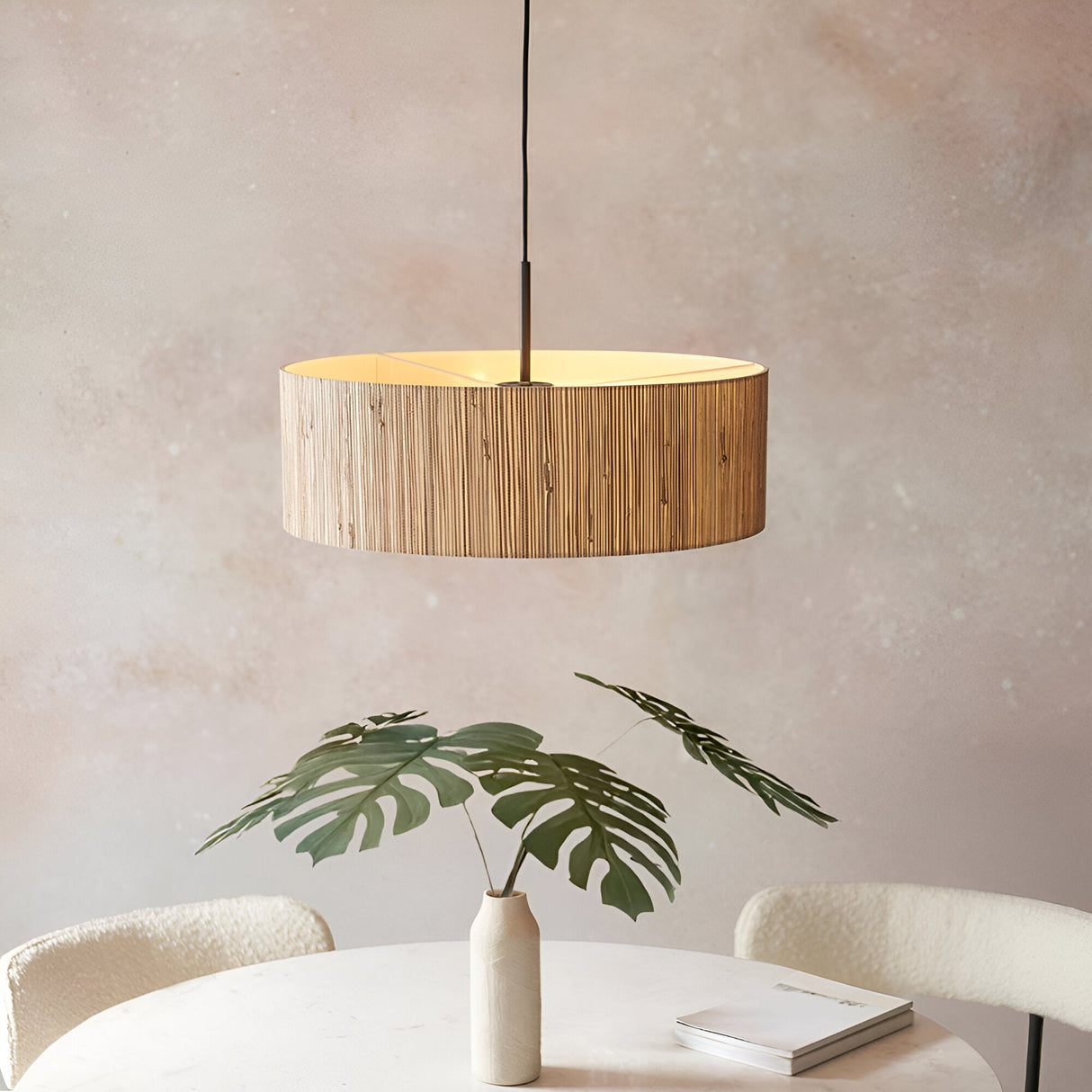 Endon Salcombe 3 light pendant with a woven natural seagrass drum shade and matt black cable, hung above a dining table with a monstera in a vase.