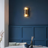 Endon Brockmont 2 light wall light in brushed aged brass with curved textured glass panel, illuminated on a deep blue panelled dining room wall.