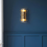 Endon Brockmont 2 light wall light illuminated on a deep blue panelled wall, with curved textured glass panel and brushed aged brass metalwork.