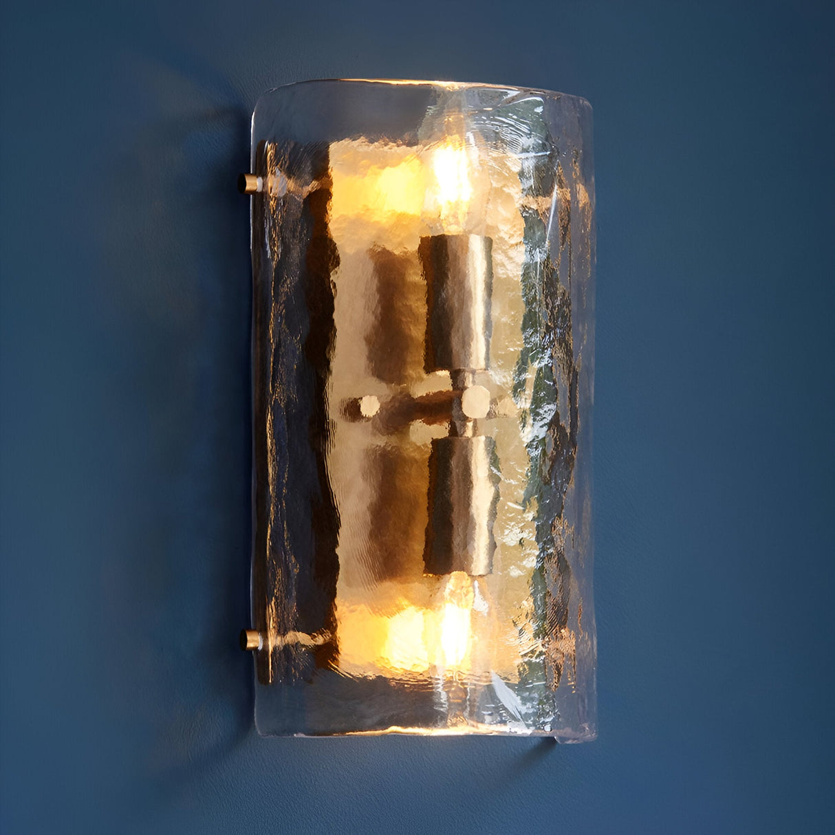 Endon Brockmont 2 light wall light with curved handmade textured glass panel and brushed aged brass metalwork, illuminated against a deep blue wall.