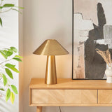 Endon Brockbourne antique brass table lamp with wide brushed conical shade on a tapered base, styled on an oak sideboard beside abstract art.