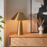 Endon Brockbourne table lamp in brushed antique brass with a wide conical shade and tapered base, styled on an oak sideboard beside a ceramic vase.