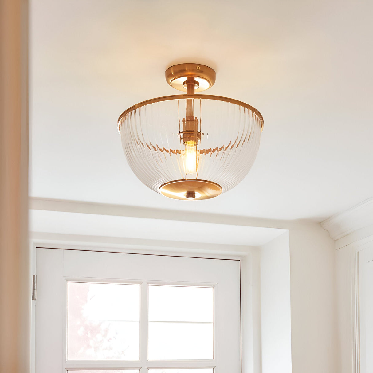 Endon Langton flush uplighter in brass with ribbed glass bowl diffuser and single E27 lamp, mounted on a white ceiling above an interior doorway.