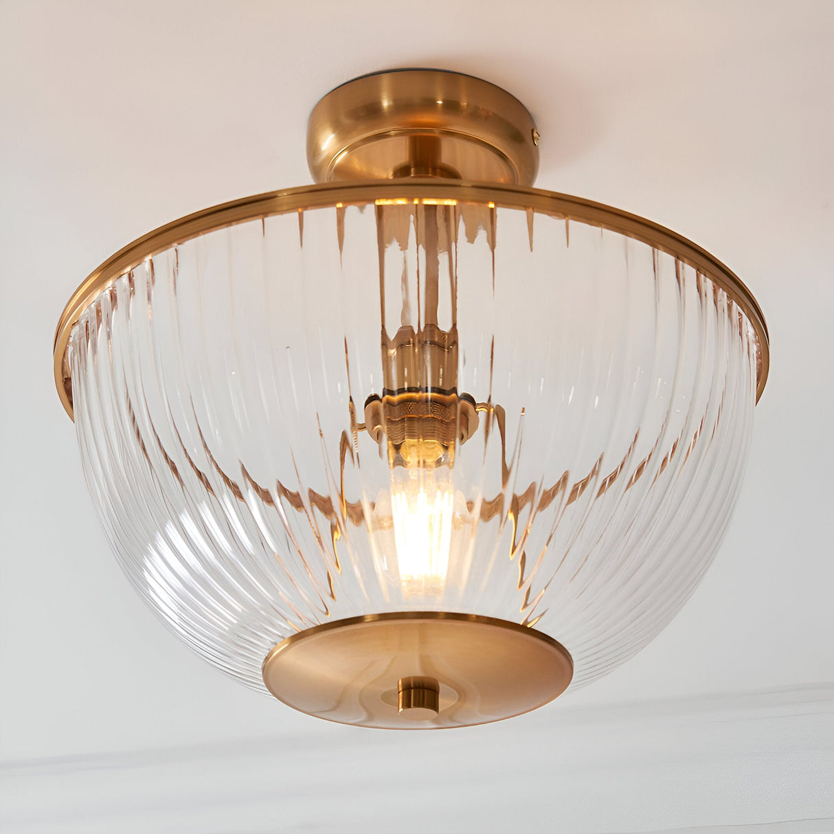 Endon Langton flush uplighter in brass with a ribbed clear glass bowl diffuser and single E27 lamp, mounted to a white ceiling.
