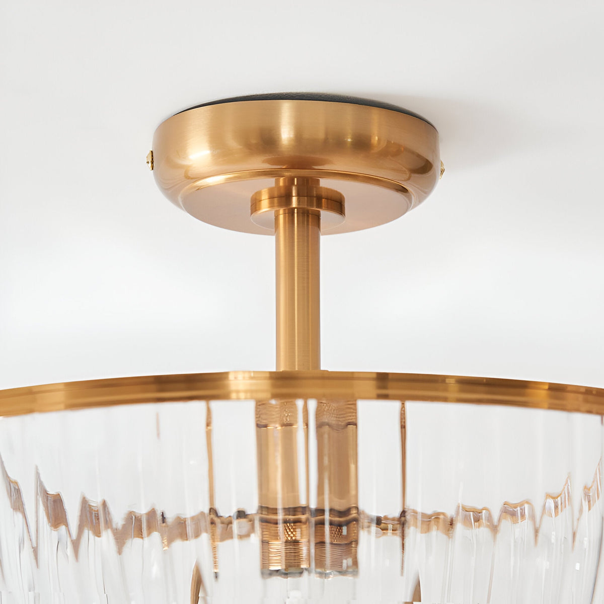 Close-up of the Endon Langton flush uplighter's brass ceiling plate, drop rod and ribbed glass diffuser rim against a white ceiling.