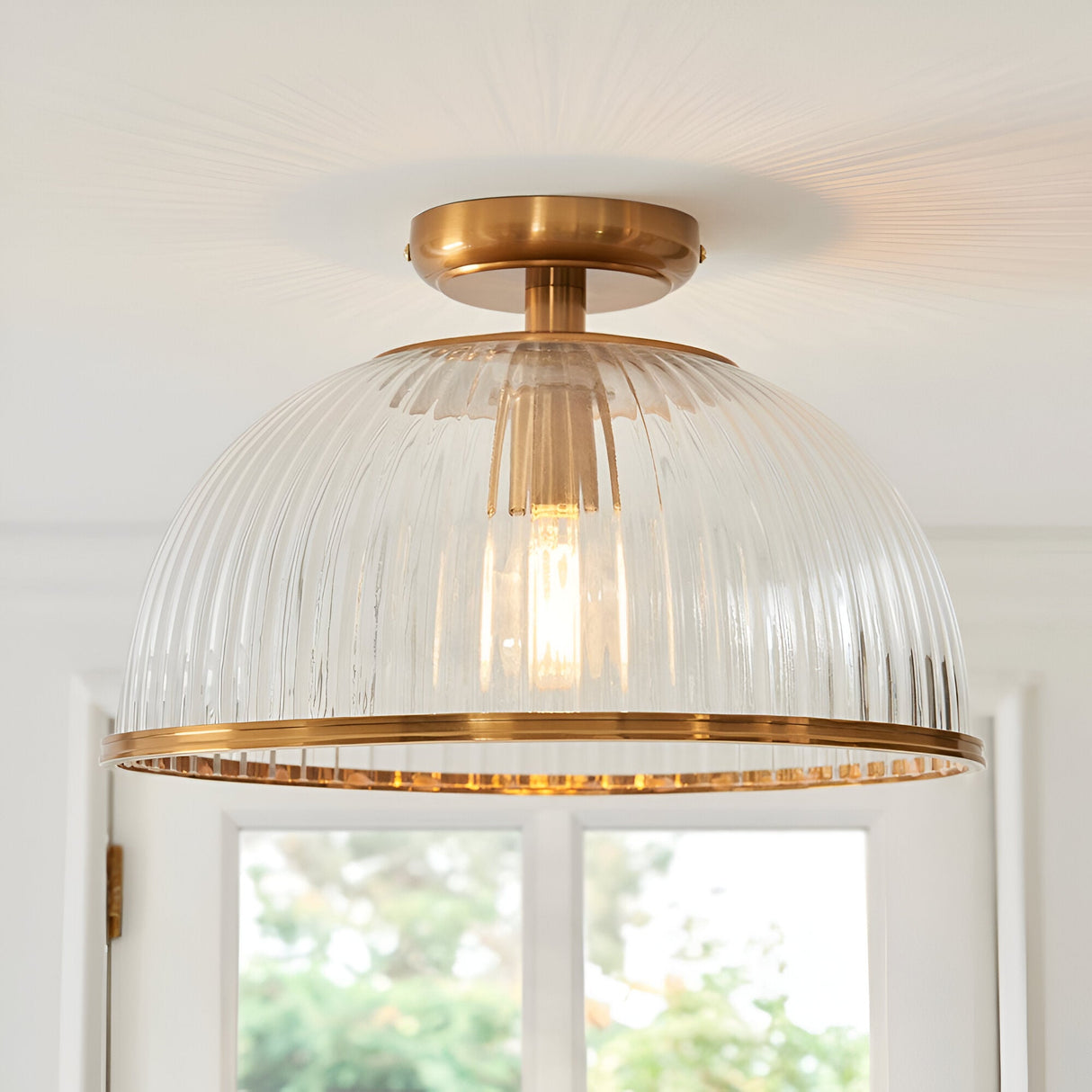 Langton Flush Downlight in brass with ribbed glass dome shade, mounted close to a white ceiling above a hallway window.