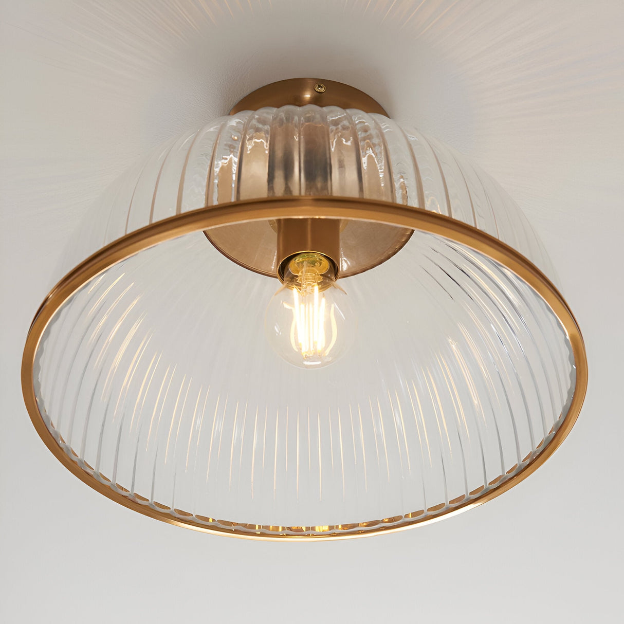 Langton Flush Downlight in brass with ribbed glass dome shade and exposed E27 bulb, mounted close to a white ceiling.