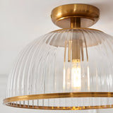 Langton flush downlight in brass, close-up of ribbed glass dome shade with brass ceiling mount and trim ring, single E27 bulb visible inside.